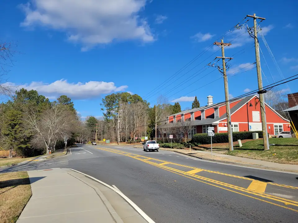 Two-lane road with a 'NORTH 372' shield, a white pickup, a red barn-style building (animal hospital sign) at right, wooded roadside and power poles, blue sky with clouds