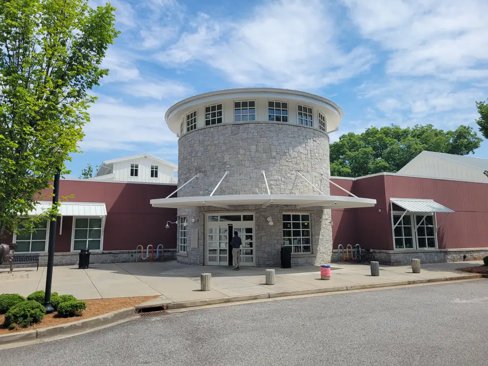 Silo-like stone entrance tower with white canopy between barn-red wings, bike racks and bollards; one patron (seen from behind, small) at the door