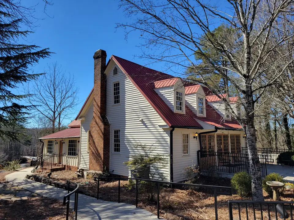 White clapboard Cape-style house with a red metal roof, three dormers, a tall brick end chimney, French doors (number 15690) and black iron railings, bare winter trees
